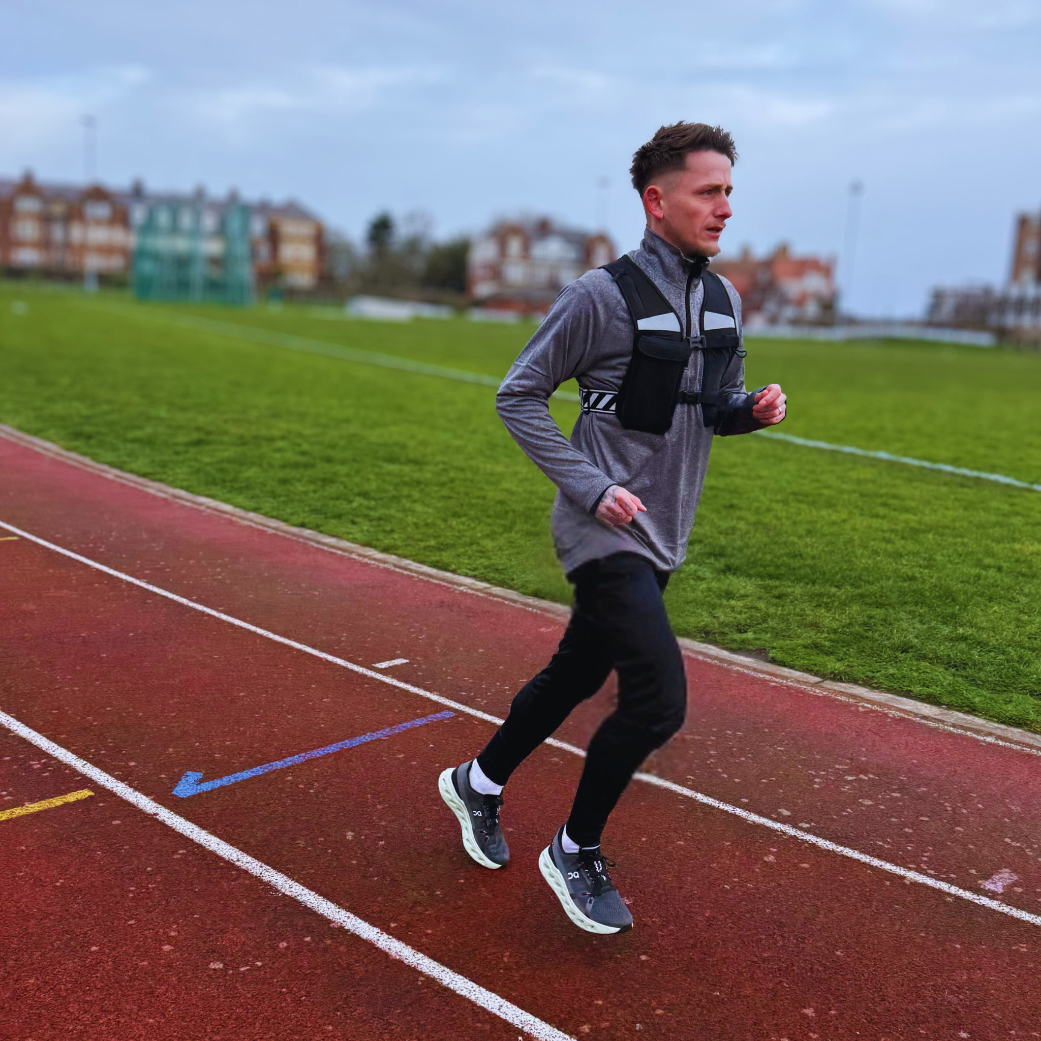 Male model running outdoors wearing black CoreVest unisex hydration running vest with reflective stripes and multiple pockets for hydration bottles, gel packs, and phone holder, designed for training, running, and active movement.