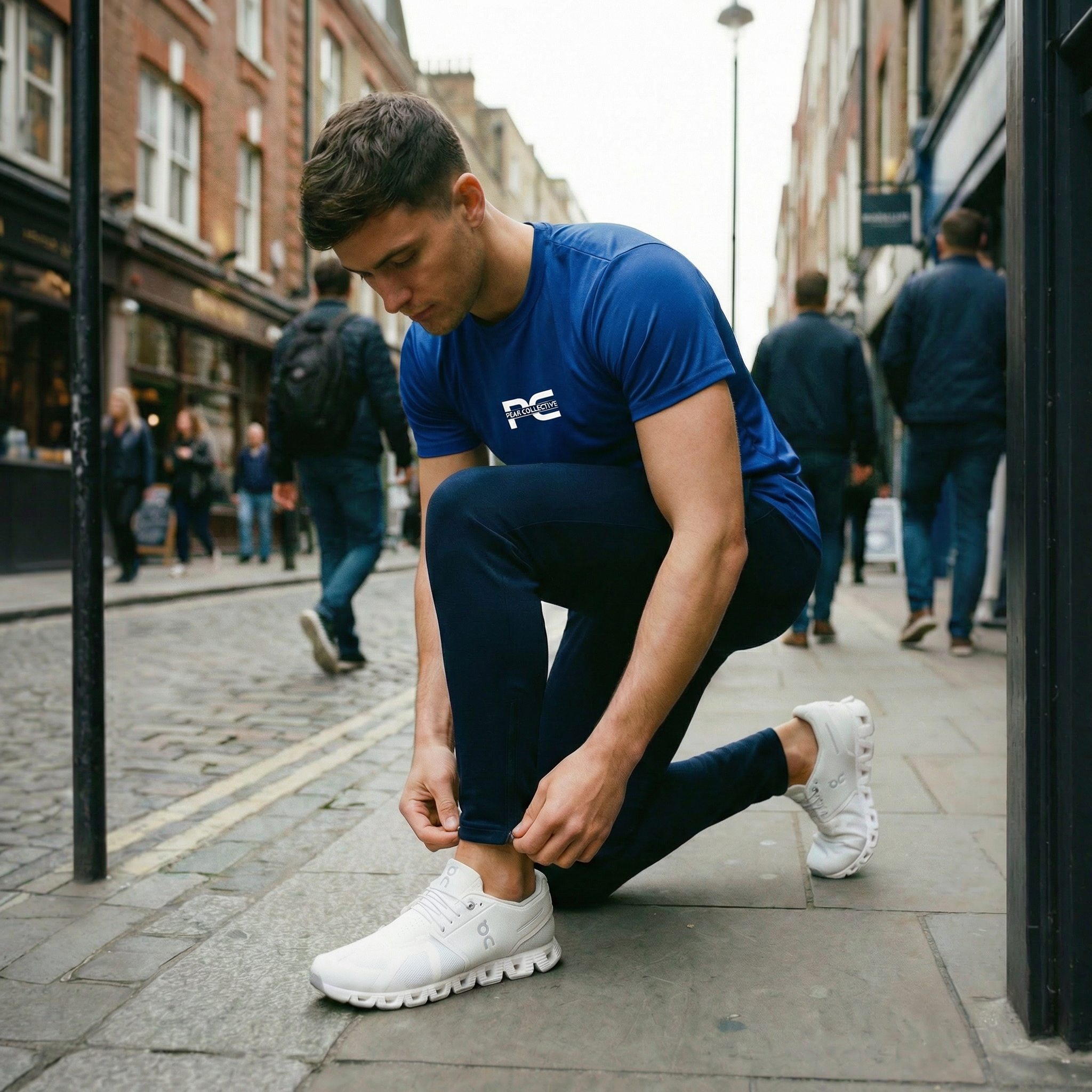 Man wearing AeroJogger men’s slim fit navy joggers with logo, adjusting the tapered hem on a city street, styled for casual and streetwear fashion.