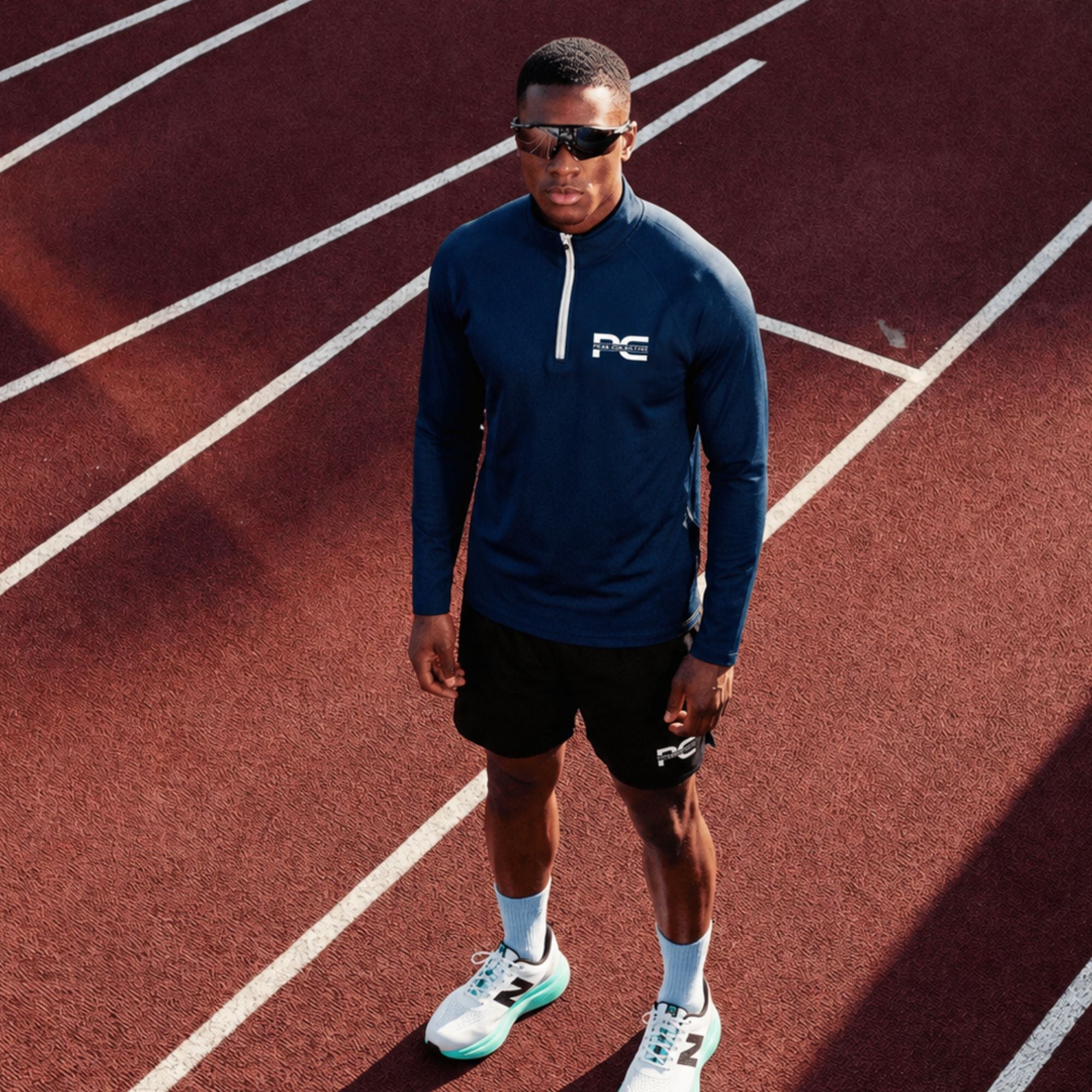 Male runner wearing navy AeroZip 1/4 performance jacket with StrideShorts double-layer running shorts on red running track – lightweight men’s activewear outfit for running, track training, jogging, and athletic performance