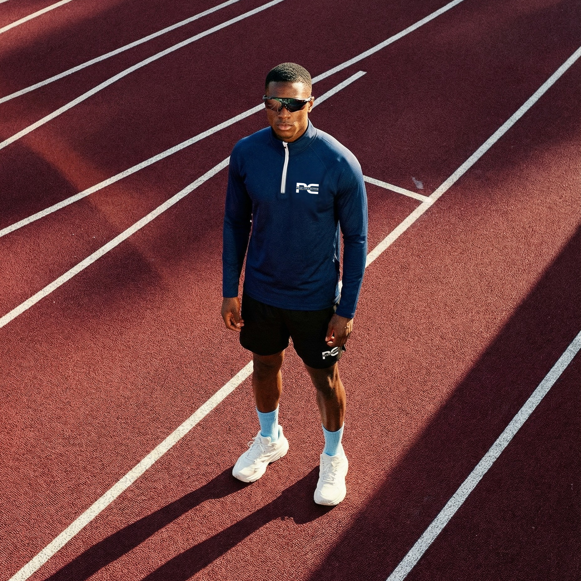 Model wearing AeroZip 1/4 long sleeve performance jacket in navy with a visible logo on a running track, designed for running, training, and active wear.
