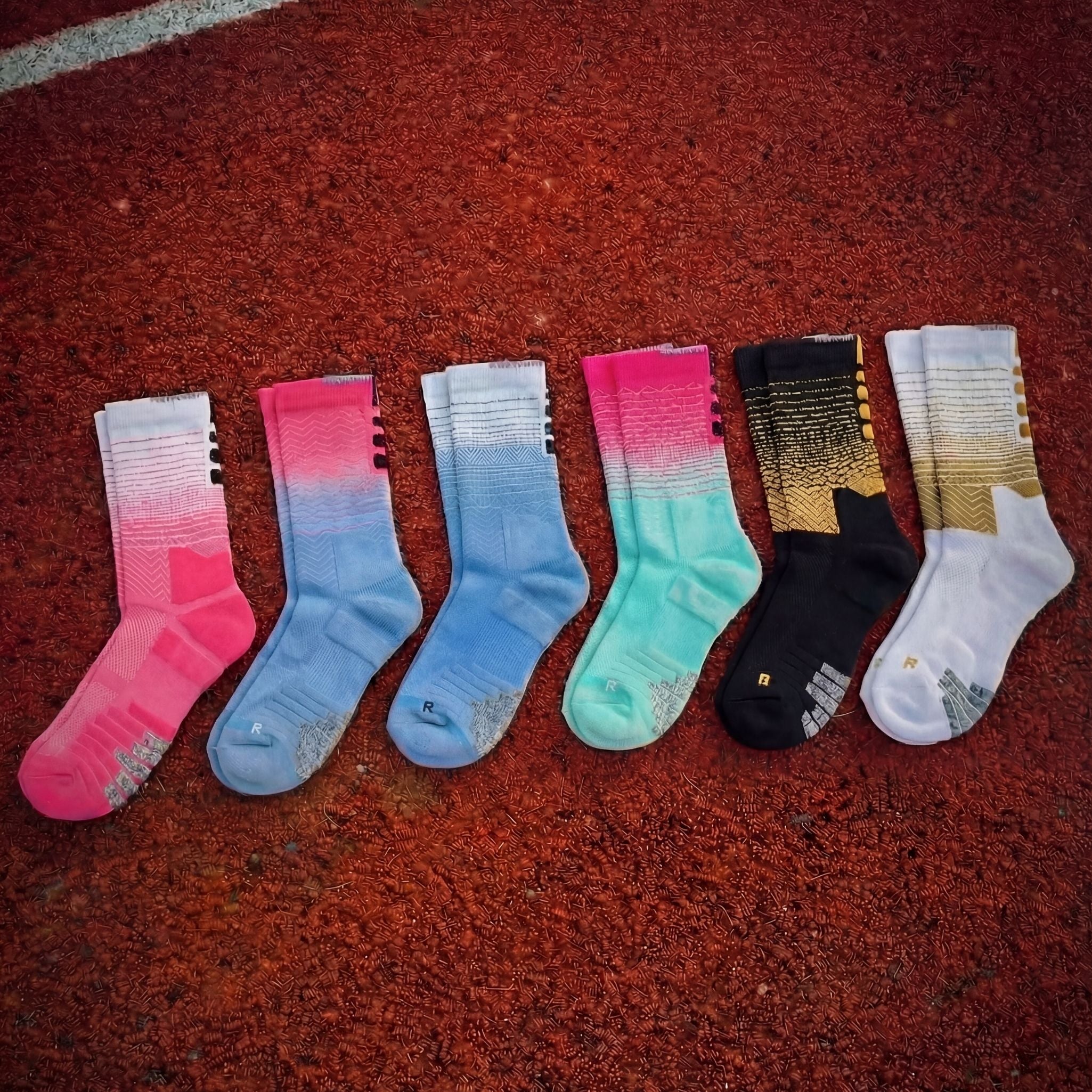 Multiple pairs of CoreStride running socks laid on a red running track. The socks are designed for runners and athletes needing cushioning, support, and moisture-wicking performance socks.