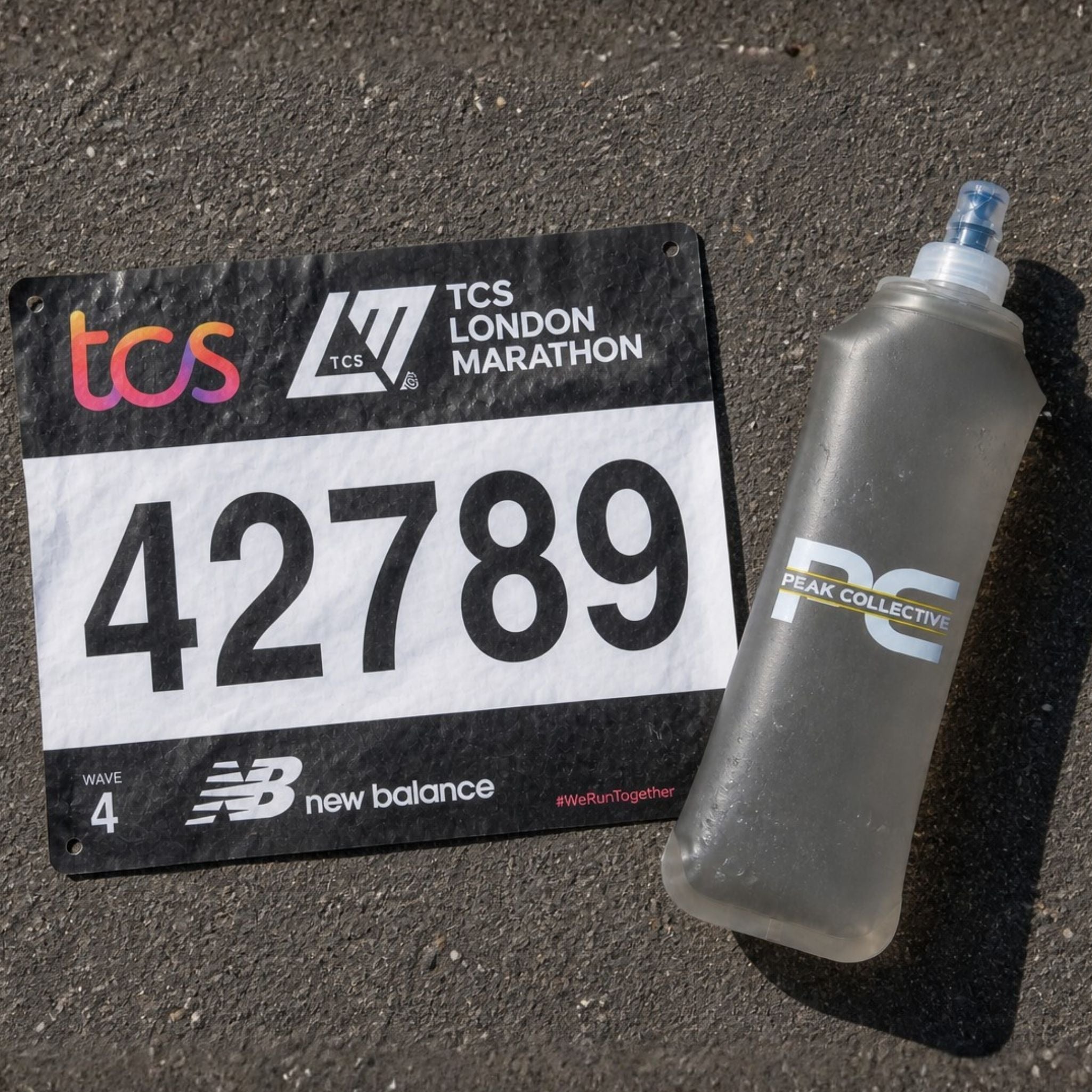 TCS London Marathon race bib with number Peak Collective PeakHydra soft flex water bottle on a dark surface.