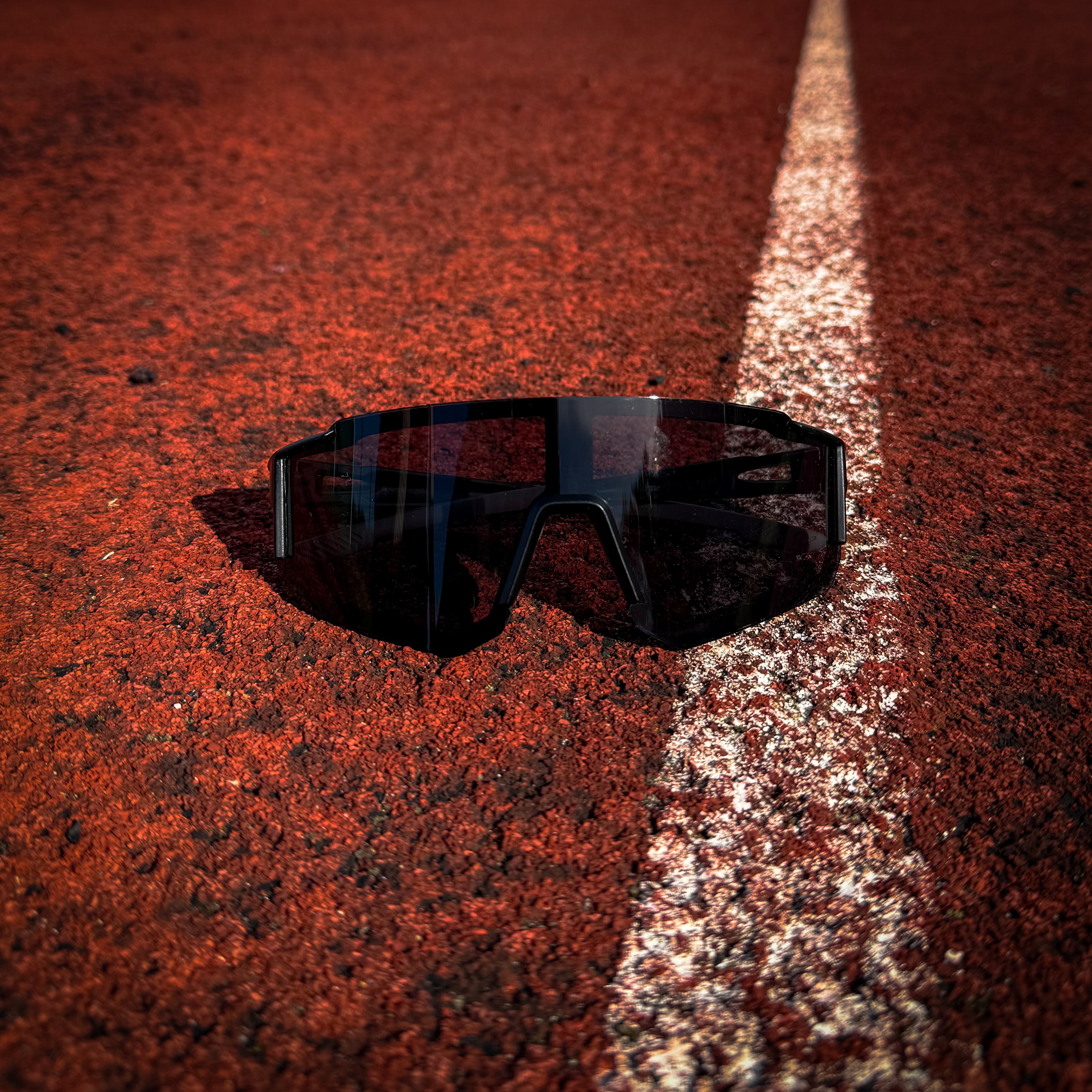 Black StormLens sports sunglasses on a red and white running track, ideal for runners needing UV protection, glare reduction, and performance eyewear.